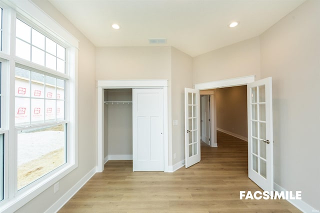 unfurnished bedroom featuring french doors, light hardwood / wood-style floors, and a closet