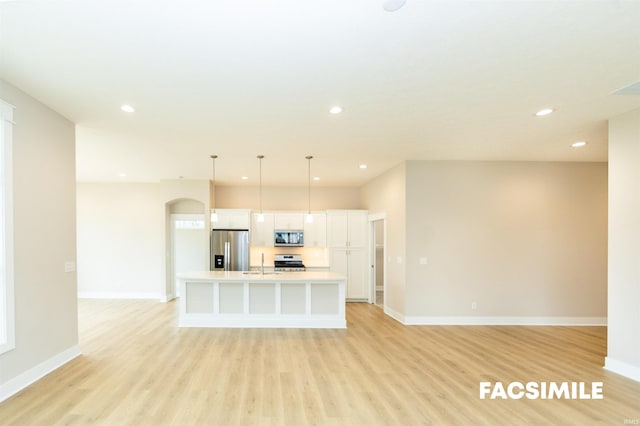 kitchen featuring sink, light wood-type flooring, hanging light fixtures, stainless steel appliances, and a kitchen island with sink