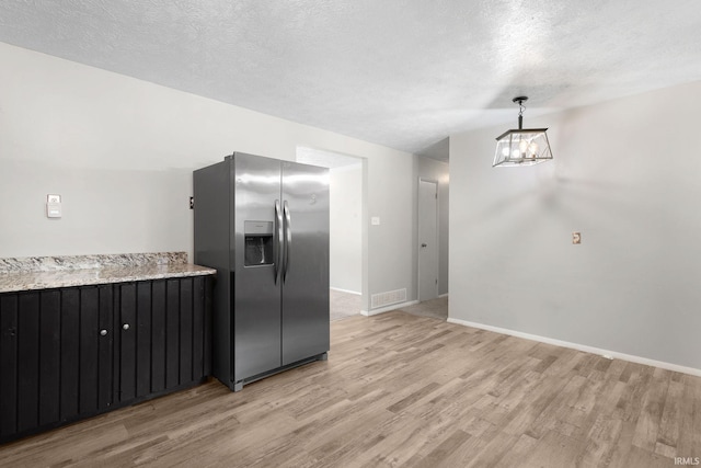 kitchen with a textured ceiling, light hardwood / wood-style floors, decorative light fixtures, light stone counters, and stainless steel refrigerator with ice dispenser