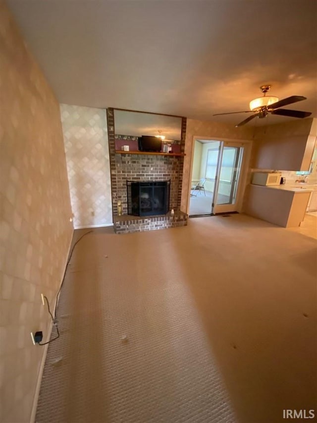 unfurnished living room featuring ceiling fan, carpet, and a brick fireplace