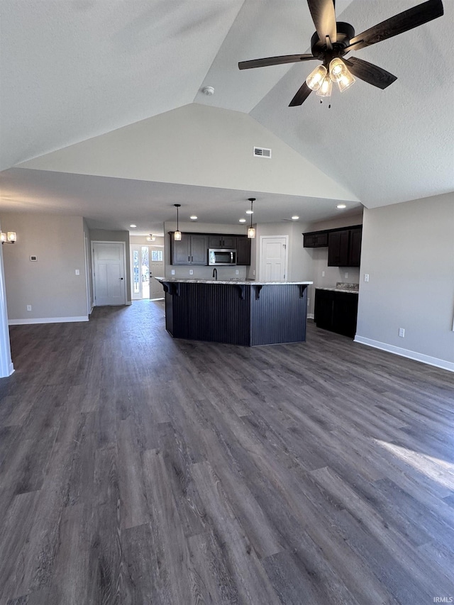 kitchen with visible vents, lofted ceiling, baseboards, open floor plan, and stainless steel microwave