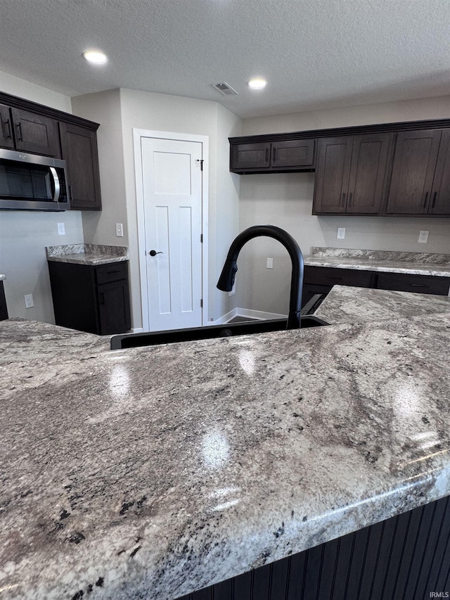 kitchen featuring dark brown cabinets, stainless steel microwave, visible vents, and a sink