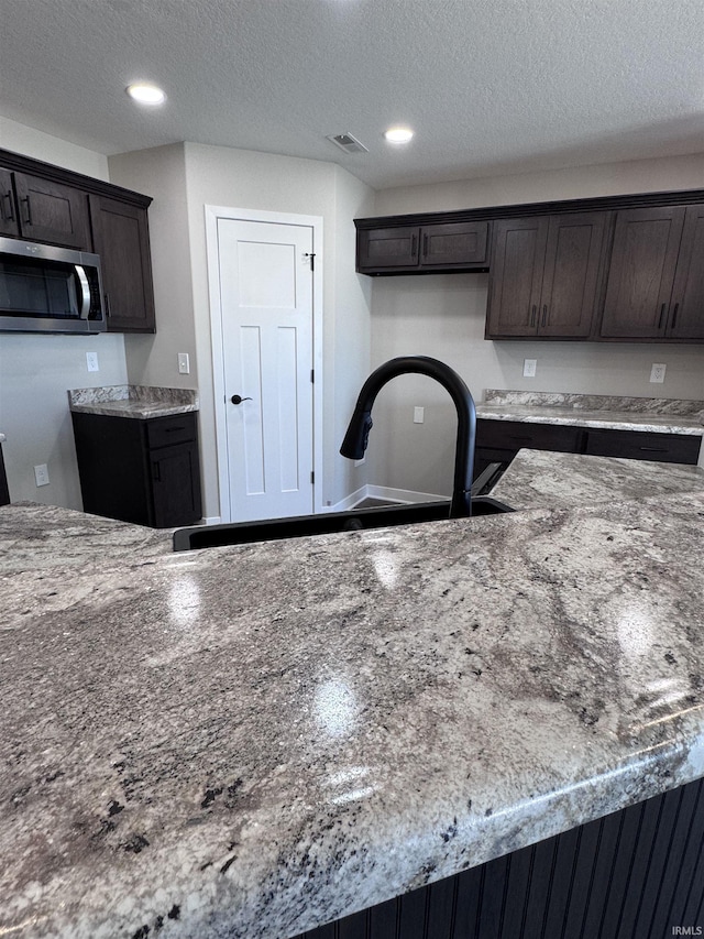 kitchen featuring a sink, stainless steel microwave, dark brown cabinetry, and visible vents