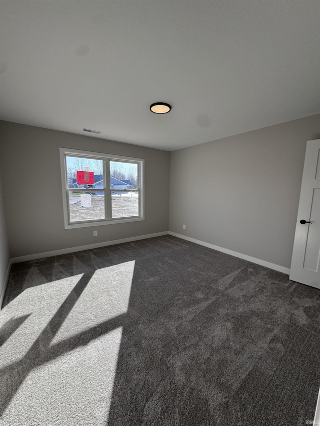 unfurnished room with baseboards, dark carpet, and visible vents