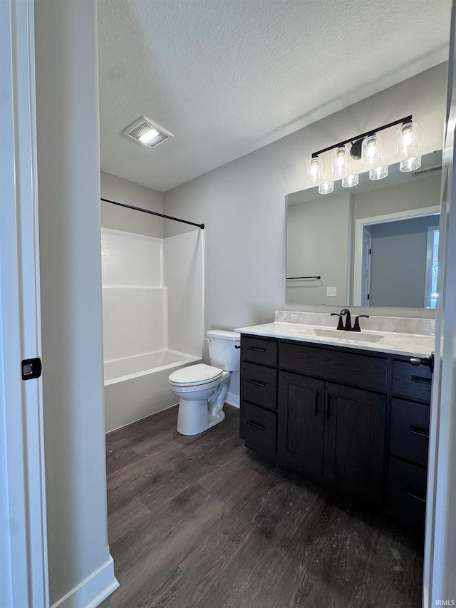 bathroom with vanity, toilet, a textured ceiling, wood finished floors, and visible vents