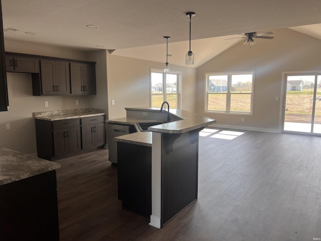 kitchen featuring a sink, a ceiling fan, baseboards, dark wood-type flooring, and a center island with sink