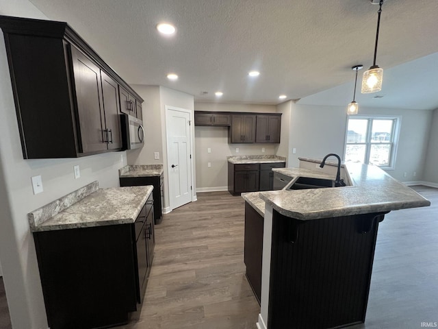 kitchen with pendant lighting, a center island with sink, sink, dark brown cabinets, and wood-type flooring