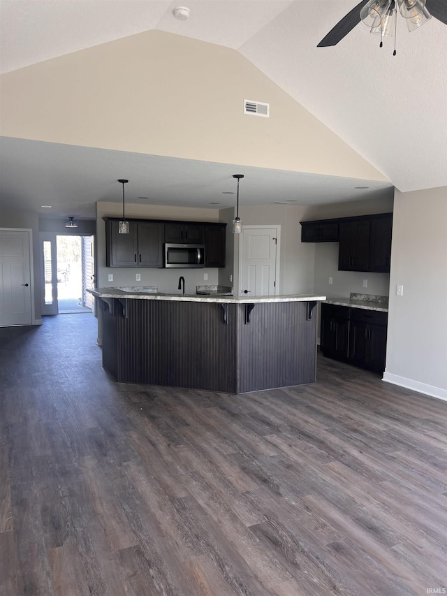 kitchen featuring visible vents, a ceiling fan, stainless steel microwave, and a breakfast bar area