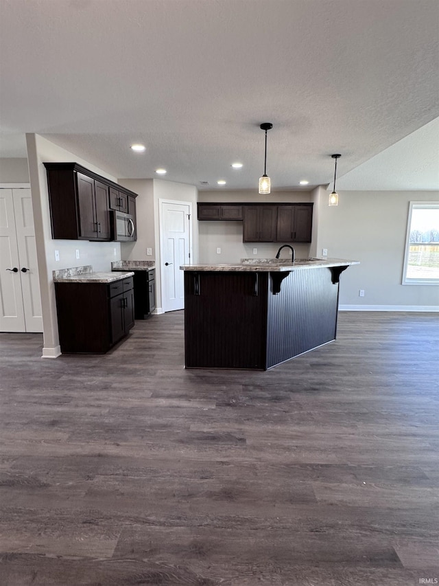 kitchen featuring dark brown cabinets, stainless steel microwave, dark wood-style floors, and baseboards