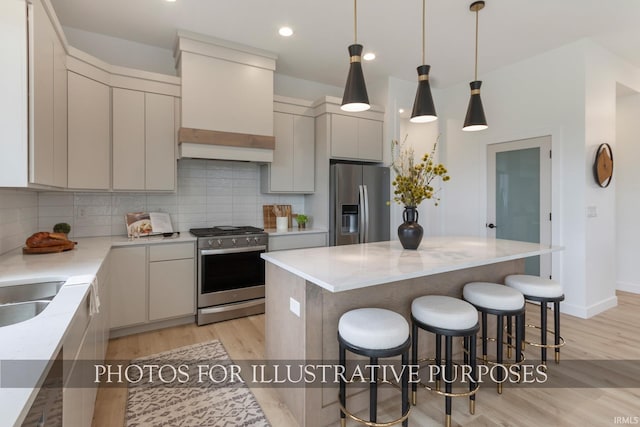 kitchen featuring appliances with stainless steel finishes, a kitchen island, backsplash, hanging light fixtures, and light hardwood / wood-style floors