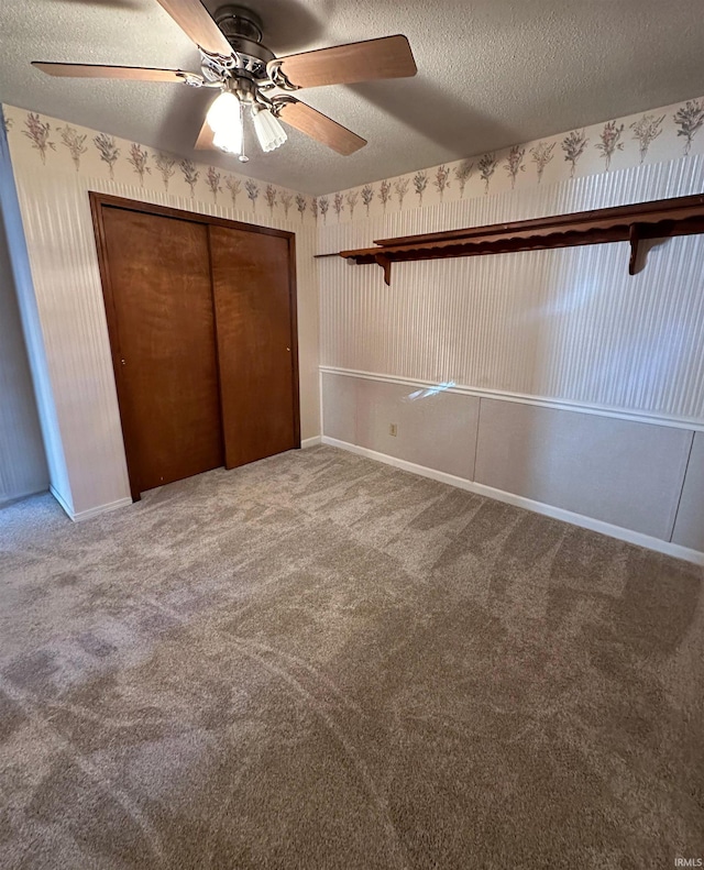 unfurnished bedroom with a closet, ceiling fan, carpet flooring, and a textured ceiling