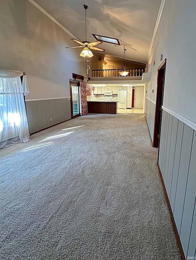 unfurnished living room featuring vaulted ceiling with skylight, a wealth of natural light, carpet flooring, and ceiling fan