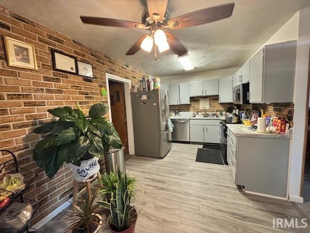 kitchen with brick wall, appliances with stainless steel finishes, light wood-type flooring, and tasteful backsplash