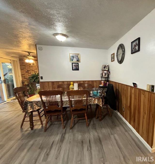 dining room featuring wood walls, a textured ceiling, dark wood-type flooring, and ceiling fan