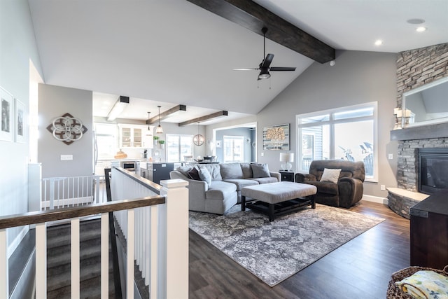 living room with dark wood-type flooring, vaulted ceiling with beams, a stone fireplace, and ceiling fan