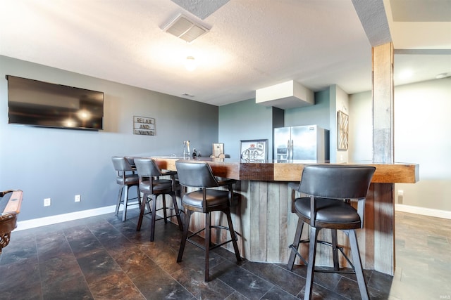 bar with stainless steel refrigerator with ice dispenser and a textured ceiling