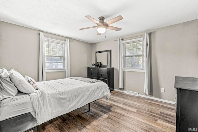 bedroom featuring light hardwood / wood-style flooring, ceiling fan, a textured ceiling, and multiple windows