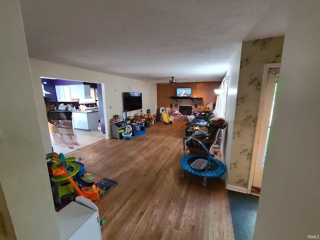 rec room featuring ceiling fan, hardwood / wood-style flooring, and a brick fireplace