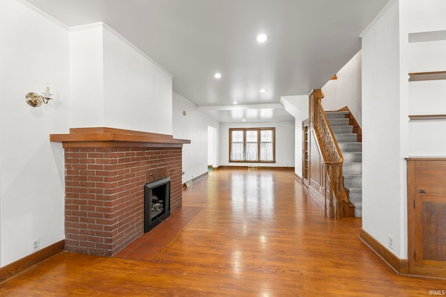 unfurnished living room with hardwood / wood-style flooring, ornamental molding, and a brick fireplace