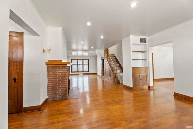 unfurnished living room featuring ornamental molding, wood-type flooring, and a brick fireplace