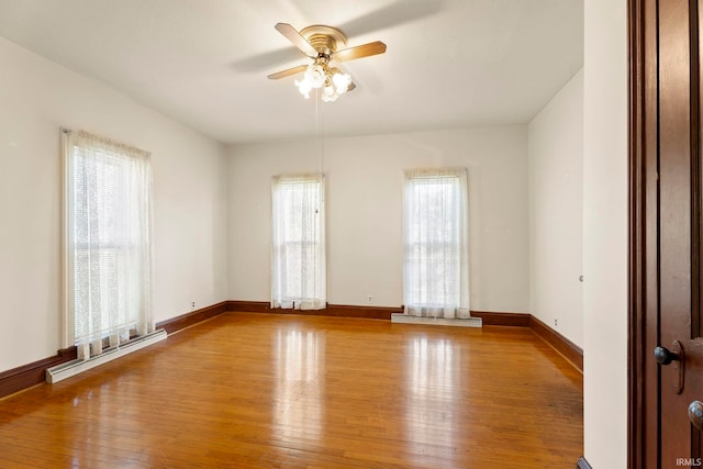 empty room with light hardwood / wood-style floors, baseboard heating, plenty of natural light, and ceiling fan