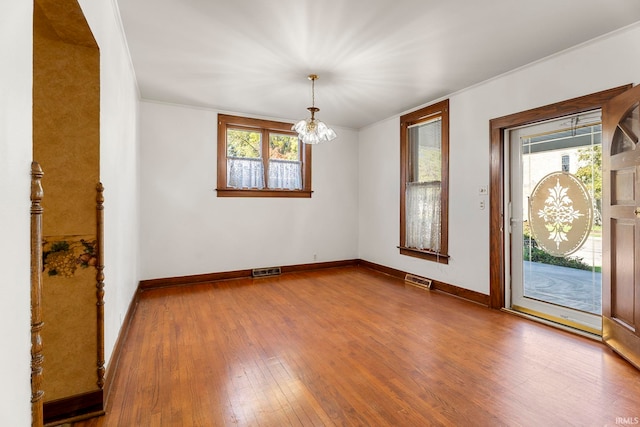 interior space featuring hardwood / wood-style flooring, a healthy amount of sunlight, ornamental molding, and a chandelier