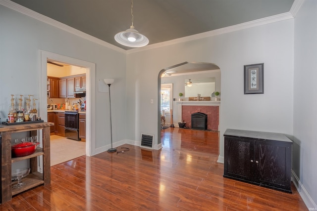 dining area featuring ceiling fan, wood-type flooring, ornamental molding, and a fireplace