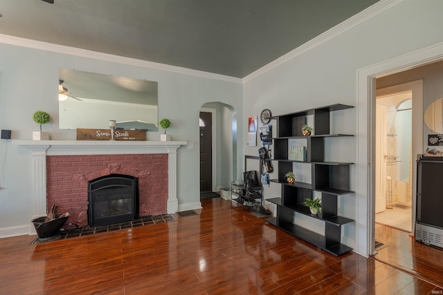 living room featuring ornamental molding, hardwood / wood-style floors, ceiling fan, and a brick fireplace