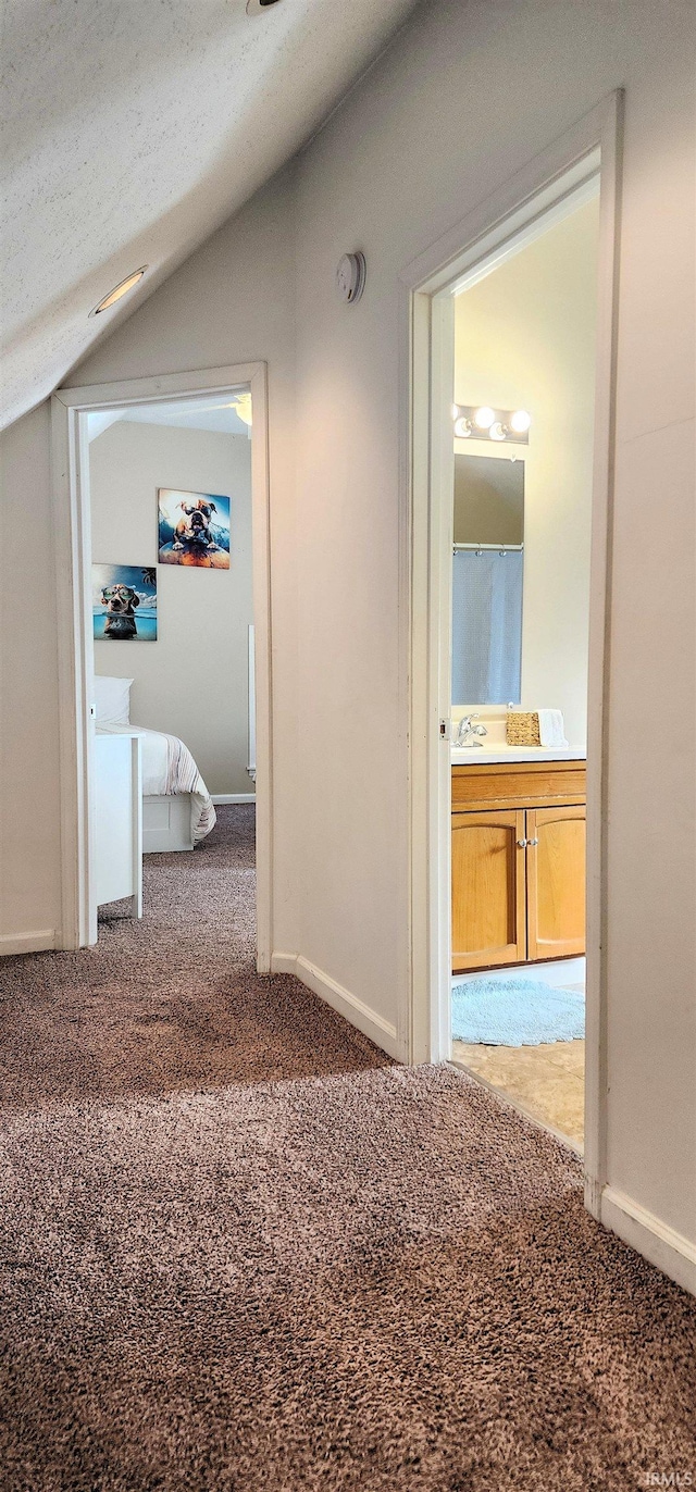 corridor with lofted ceiling, a textured ceiling, and carpet flooring