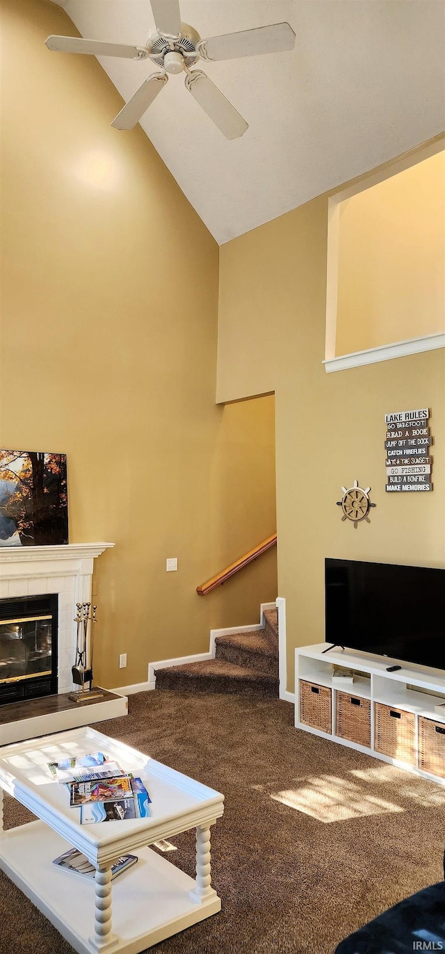 living room with a tiled fireplace, ceiling fan, high vaulted ceiling, and carpet