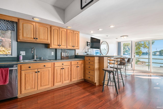 kitchen with sink, a kitchen bar, dark hardwood / wood-style flooring, kitchen peninsula, and stainless steel dishwasher