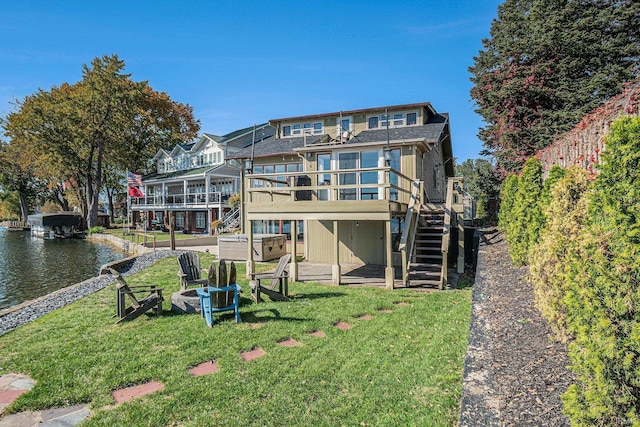 rear view of house featuring a deck with water view and a lawn