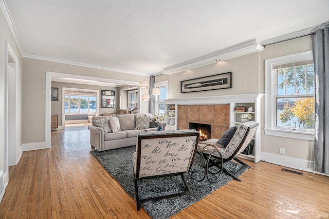 living room with a wealth of natural light, crown molding, wood-type flooring, and a tile fireplace