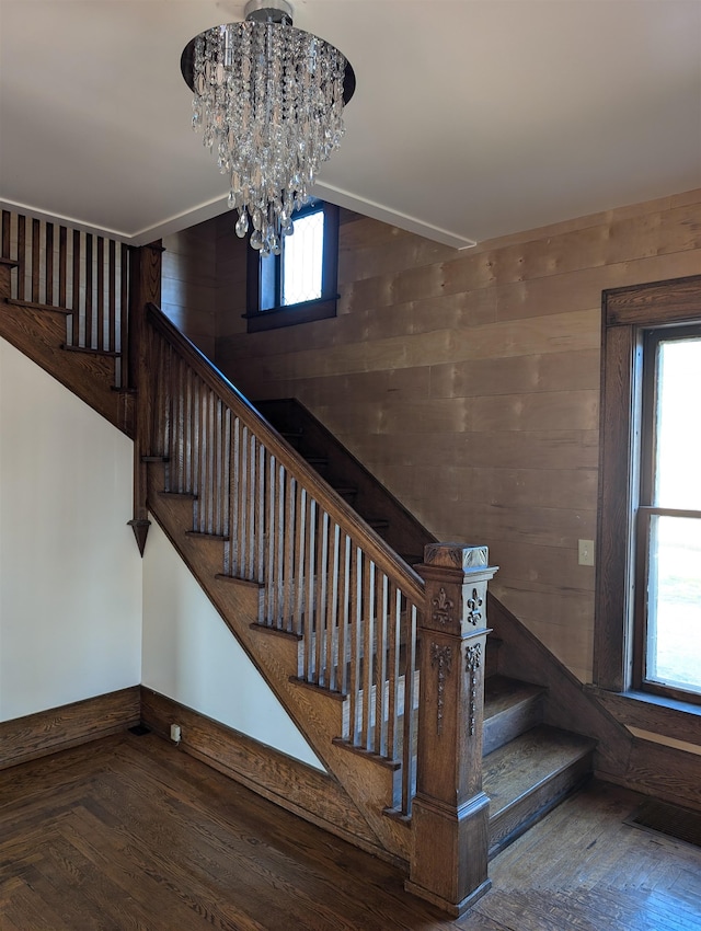 stairs with a notable chandelier, parquet floors, and wood walls