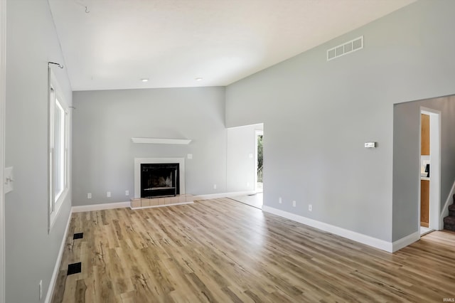 unfurnished living room featuring light hardwood / wood-style flooring, high vaulted ceiling, and a tile fireplace