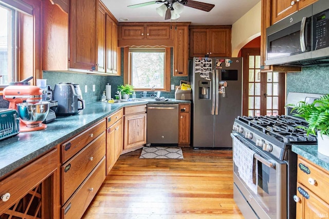 kitchen with stainless steel appliances, sink, ceiling fan, light wood-type flooring, and decorative backsplash