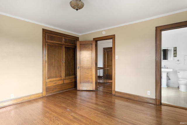 unfurnished bedroom featuring hardwood / wood-style floors, ornamental molding, and ensuite bath