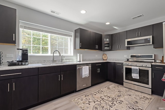 kitchen with sink, light stone counters, stainless steel appliances, and light hardwood / wood-style floors