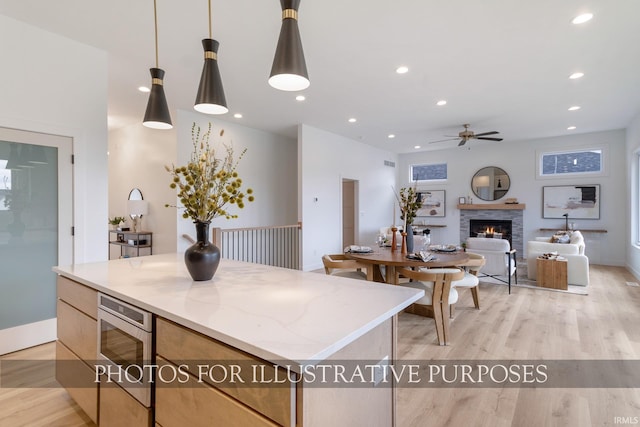 kitchen featuring a fireplace, a center island, pendant lighting, light stone counters, and light hardwood / wood-style flooring