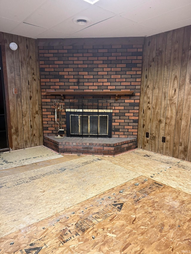 unfurnished living room featuring wooden walls and a brick fireplace