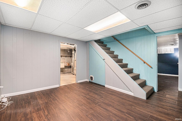 basement featuring a drop ceiling, dark hardwood / wood-style floors, and wood walls