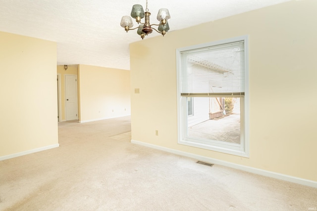 unfurnished room with a textured ceiling, light carpet, and an inviting chandelier