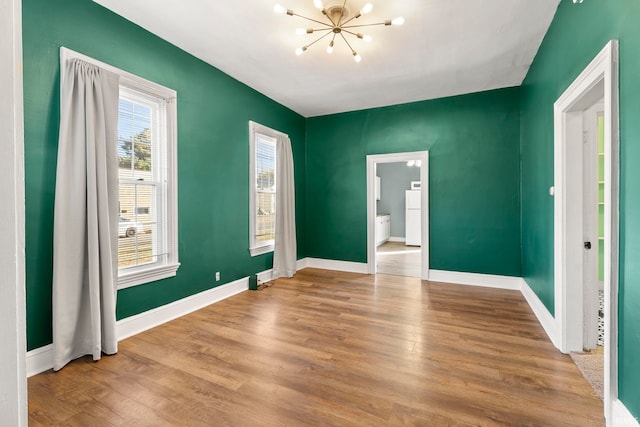 empty room featuring wood-type flooring and an inviting chandelier