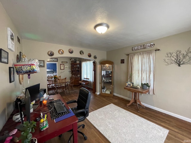 office area featuring baseboards, arched walkways, and wood finished floors