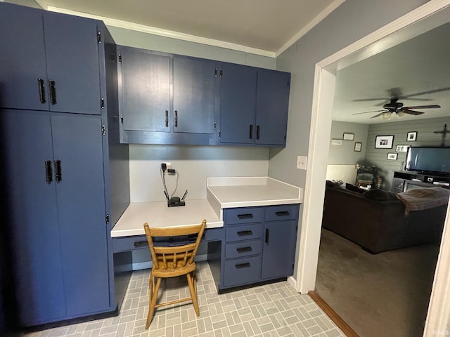 kitchen with a ceiling fan, blue cabinetry, built in study area, light countertops, and ornamental molding