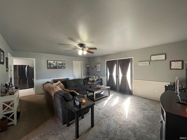 carpeted living area with a ceiling fan and wainscoting