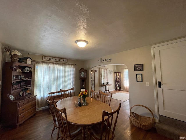 dining area featuring arched walkways, dark wood-style flooring, and a wealth of natural light