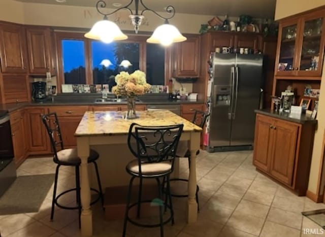 kitchen with hanging light fixtures, stainless steel appliances, a center island, light tile patterned flooring, and light stone counters