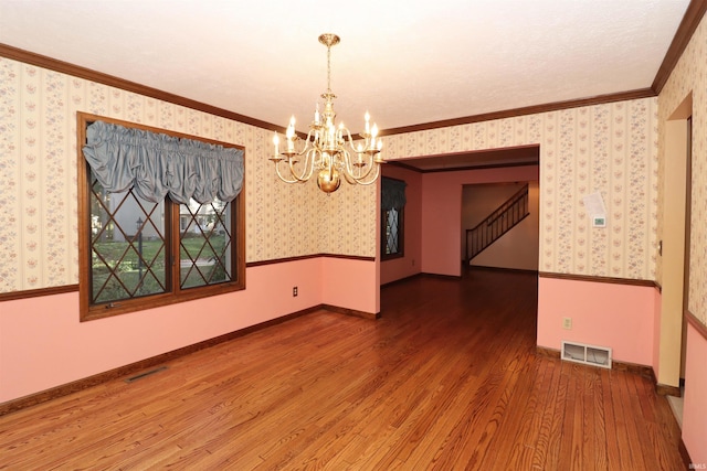 empty room with ornamental molding, hardwood / wood-style floors, and an inviting chandelier