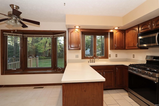 kitchen featuring kitchen peninsula, ceiling fan, appliances with stainless steel finishes, light tile patterned flooring, and sink